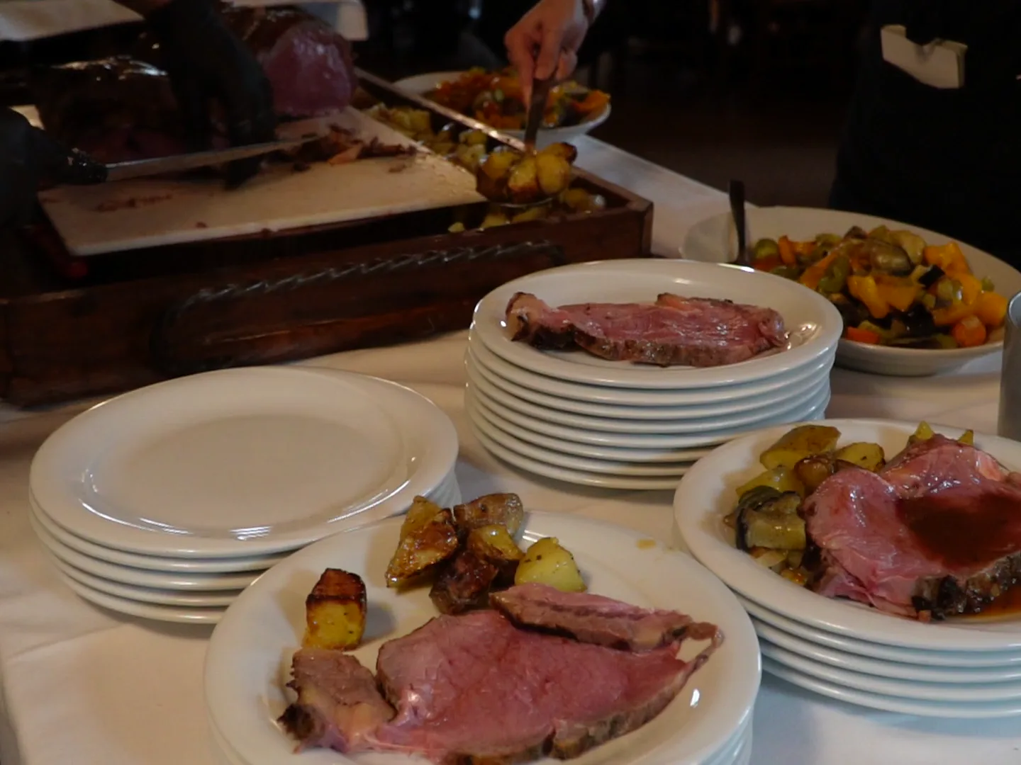 Plato de banquete terminado con lonjas de carne, papas doradas y salsa, junto a pilas de vajilla lista para el servicio.