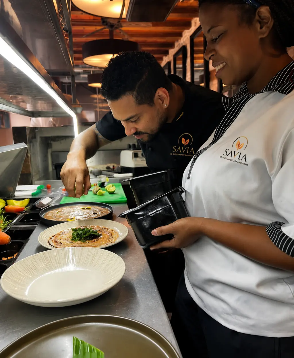 Chef terminando el emplatado de un plato junto a una integrante del equipo de cocina.