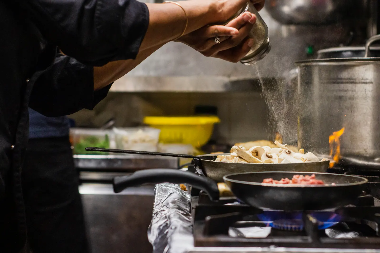 Cocinero salteando en sartén sobre fuego vivo durante un servicio.