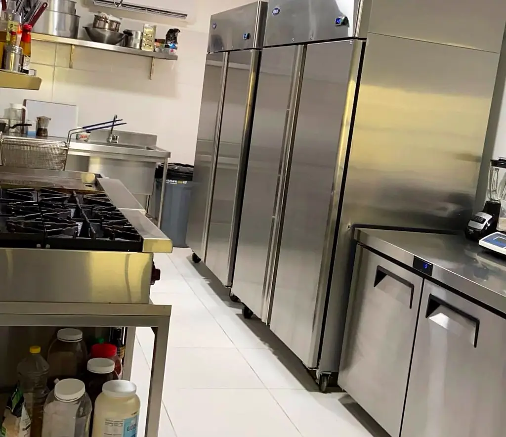 Cocina industrial equipada con estufa de volumen, campana de extracción y mesones en acero inoxidable.