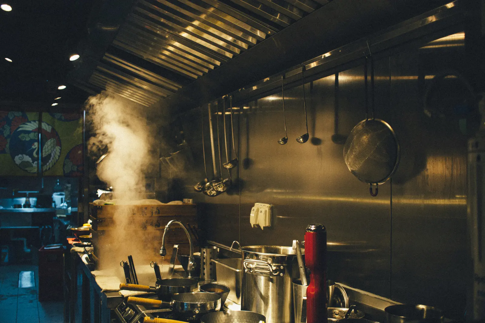 Cocina industrial en plena producción, con vapor saliendo de las marmitas.
