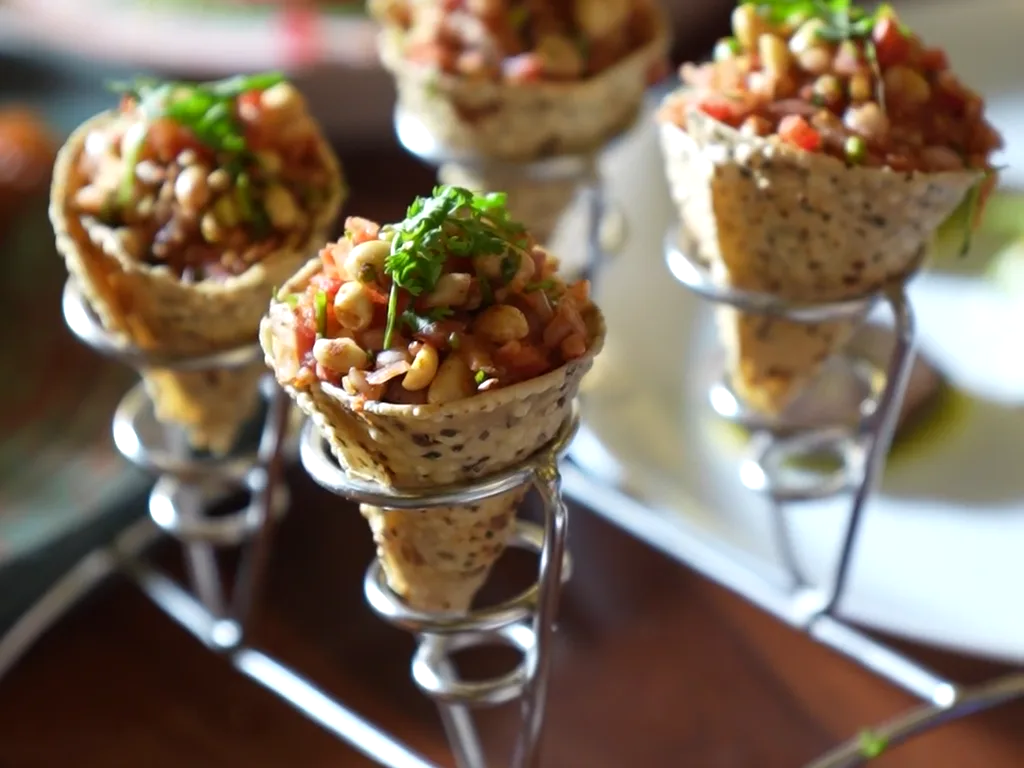 Conos de masa crujiente rellenos de tartar y hierbas frescas, servidos en soporte metálico sobre una mesa de madera.