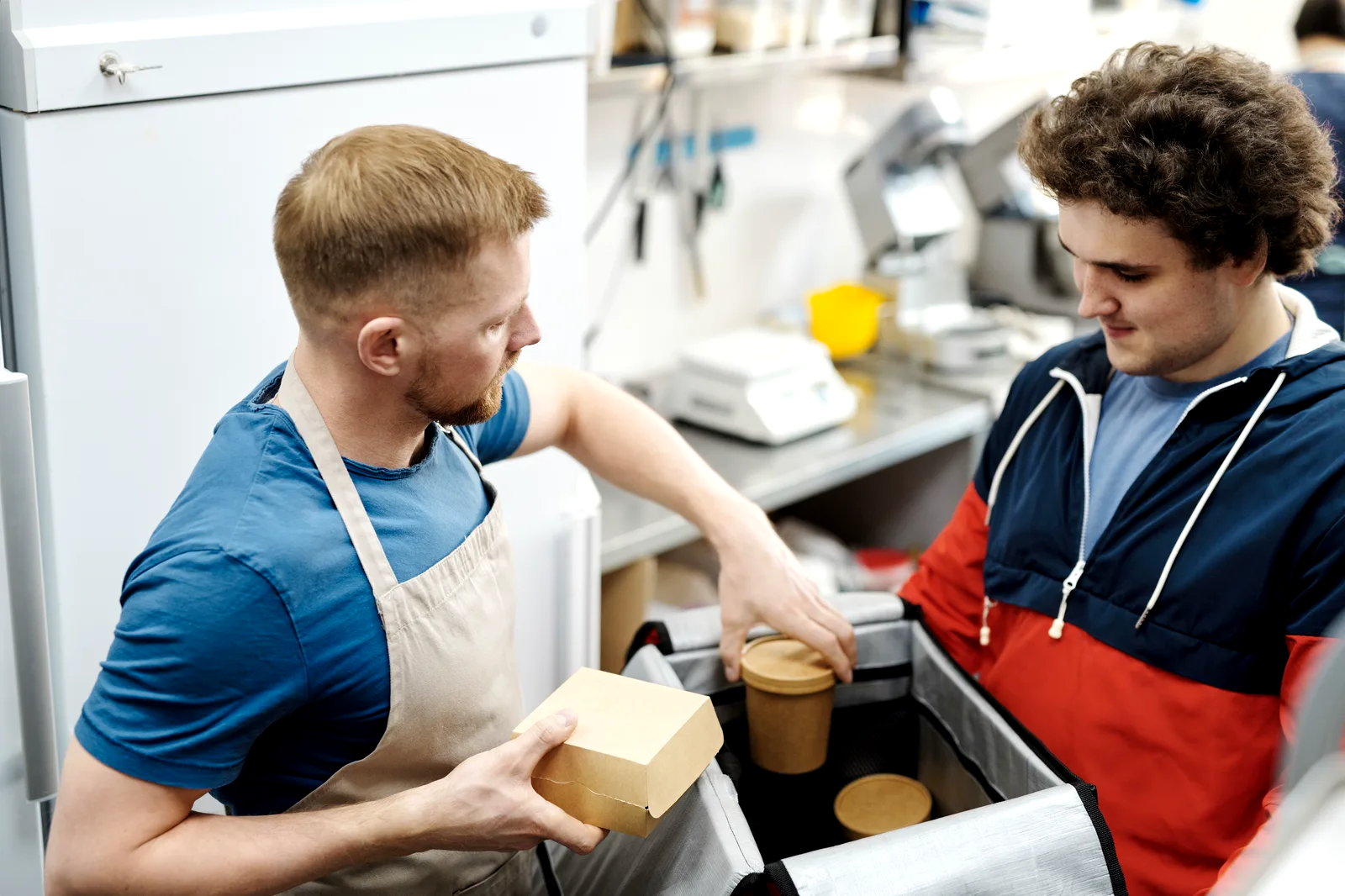 A lunch order in a cardboard box being packed into an insulated bag for delivery.