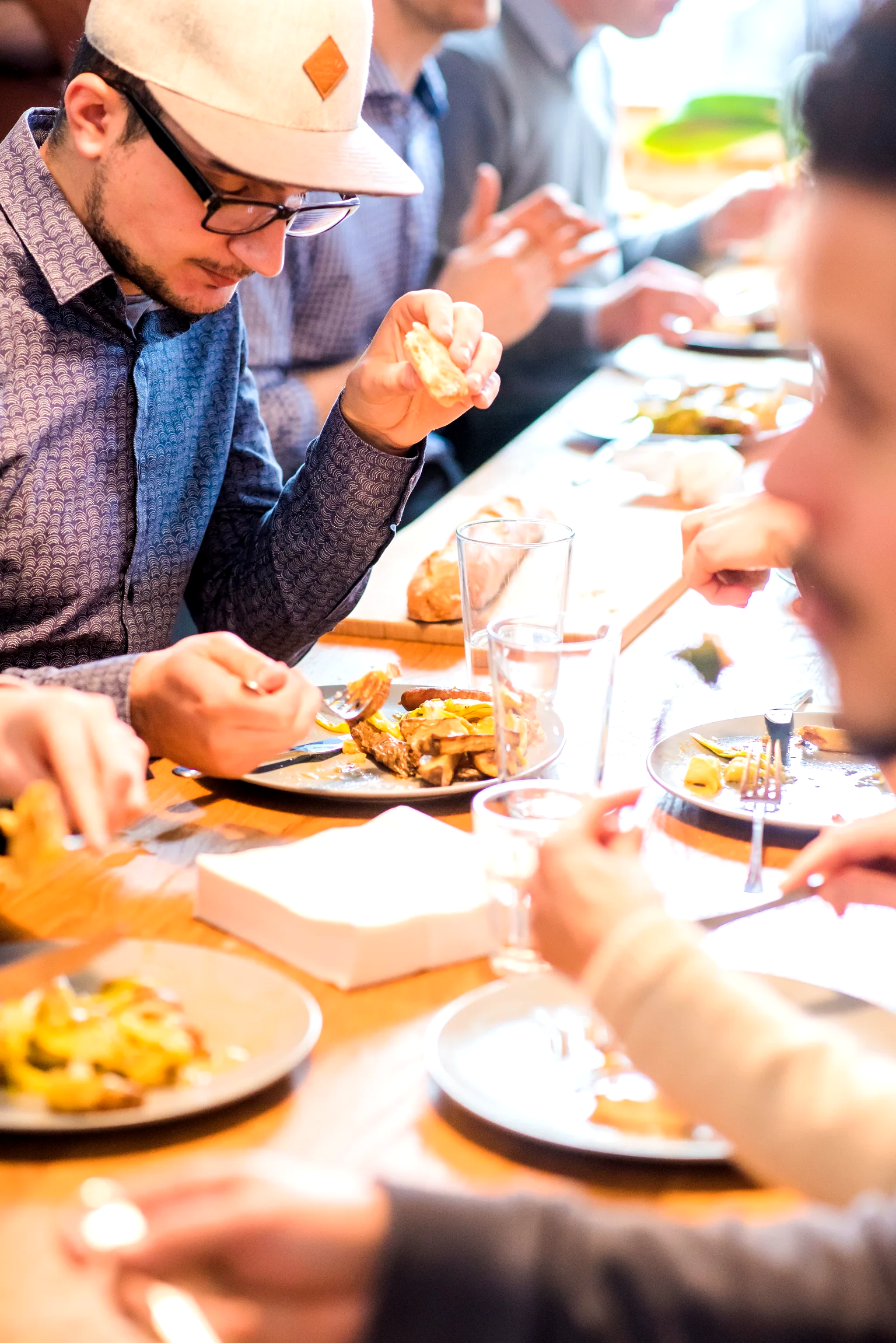 Mesa larga de oficina a la hora del almuerzo, con varias personas comiendo su plato servido.