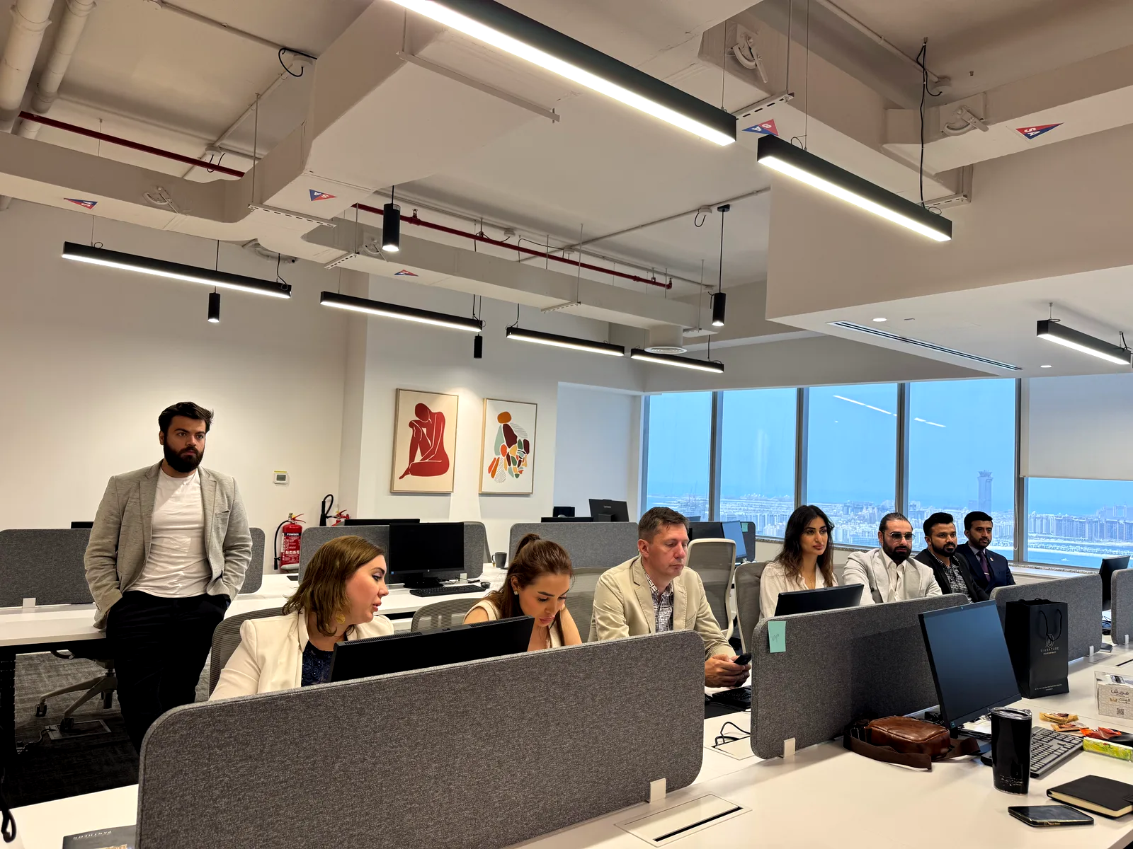 Equipo de trabajo en una oficina de planta abierta con ventanal corrido y vista a la ciudad.