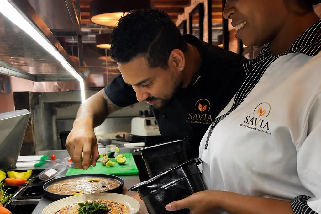 El chef ejecutivo y una integrante del equipo terminando el emplatado de un plato en cocina, con uniforme SAVIA.