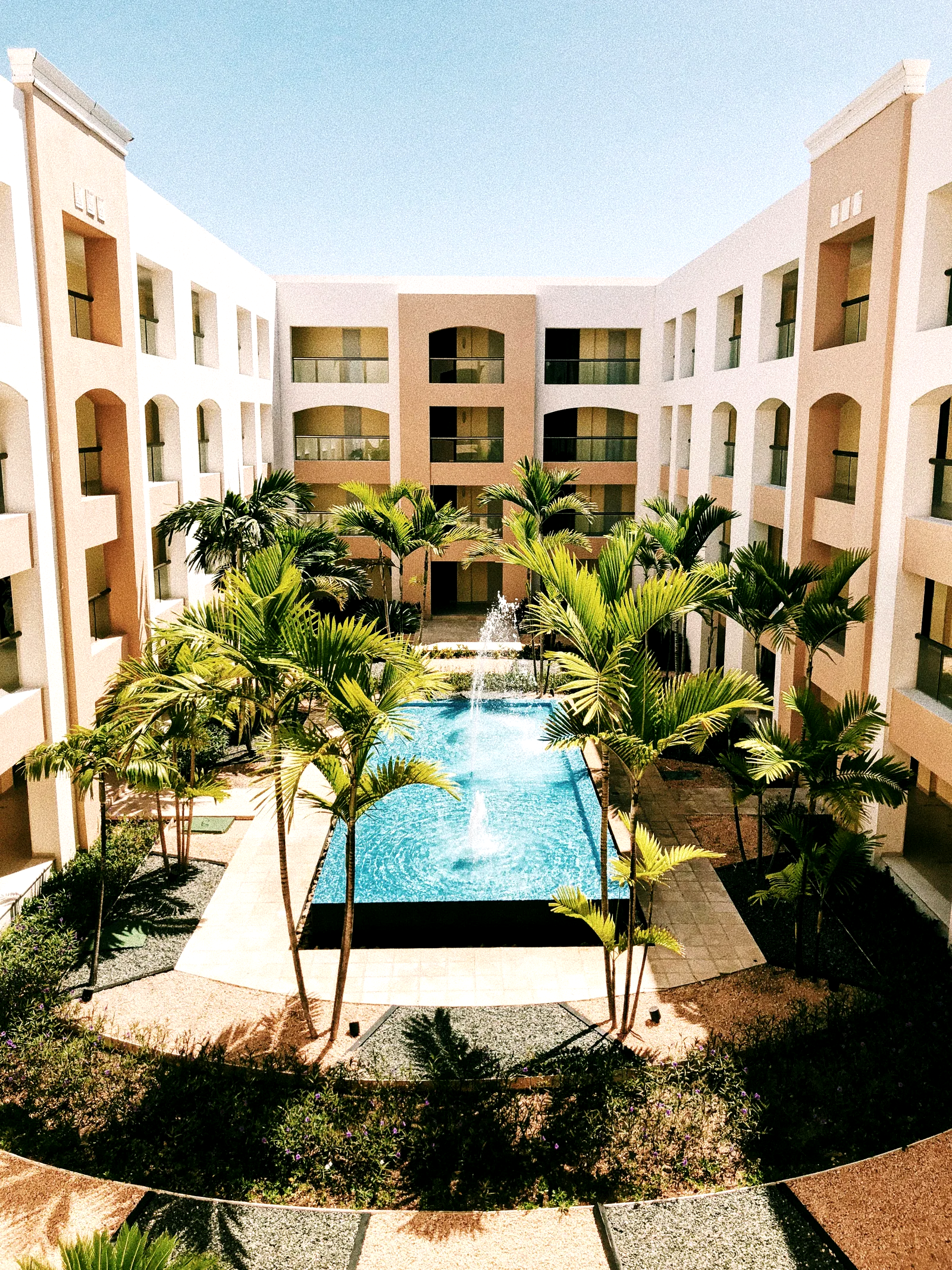 Claustro de un hotel con piscina y fuente central, rodeado de palmeras y galerías en arco.