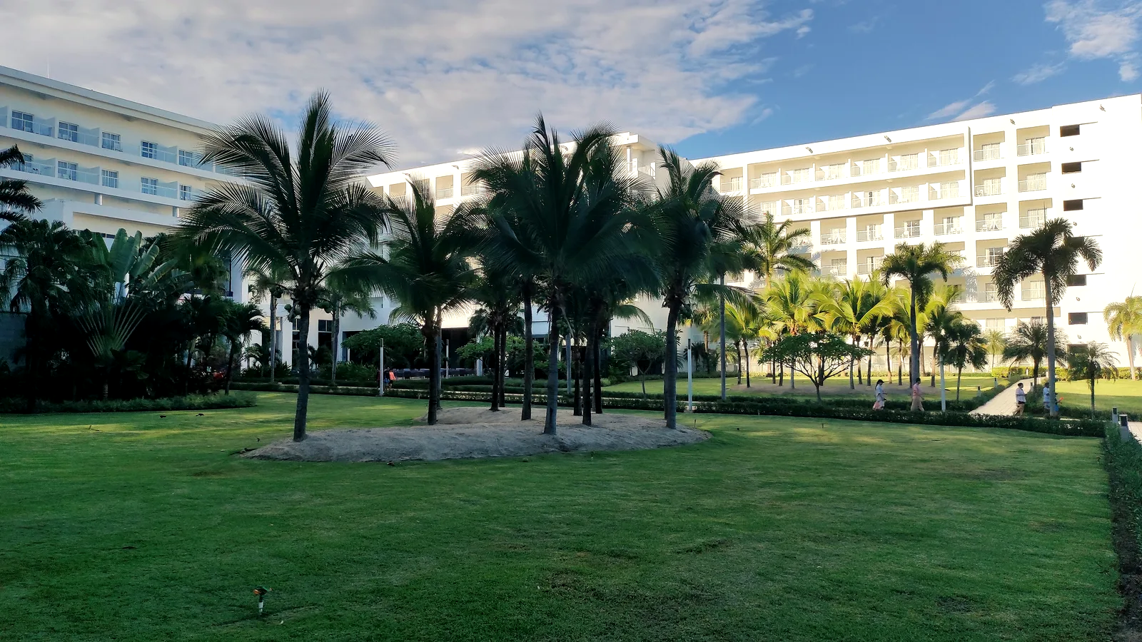 Jardín central de un complejo hotelero al amanecer, con palmeras entre dos bloques de habitaciones.