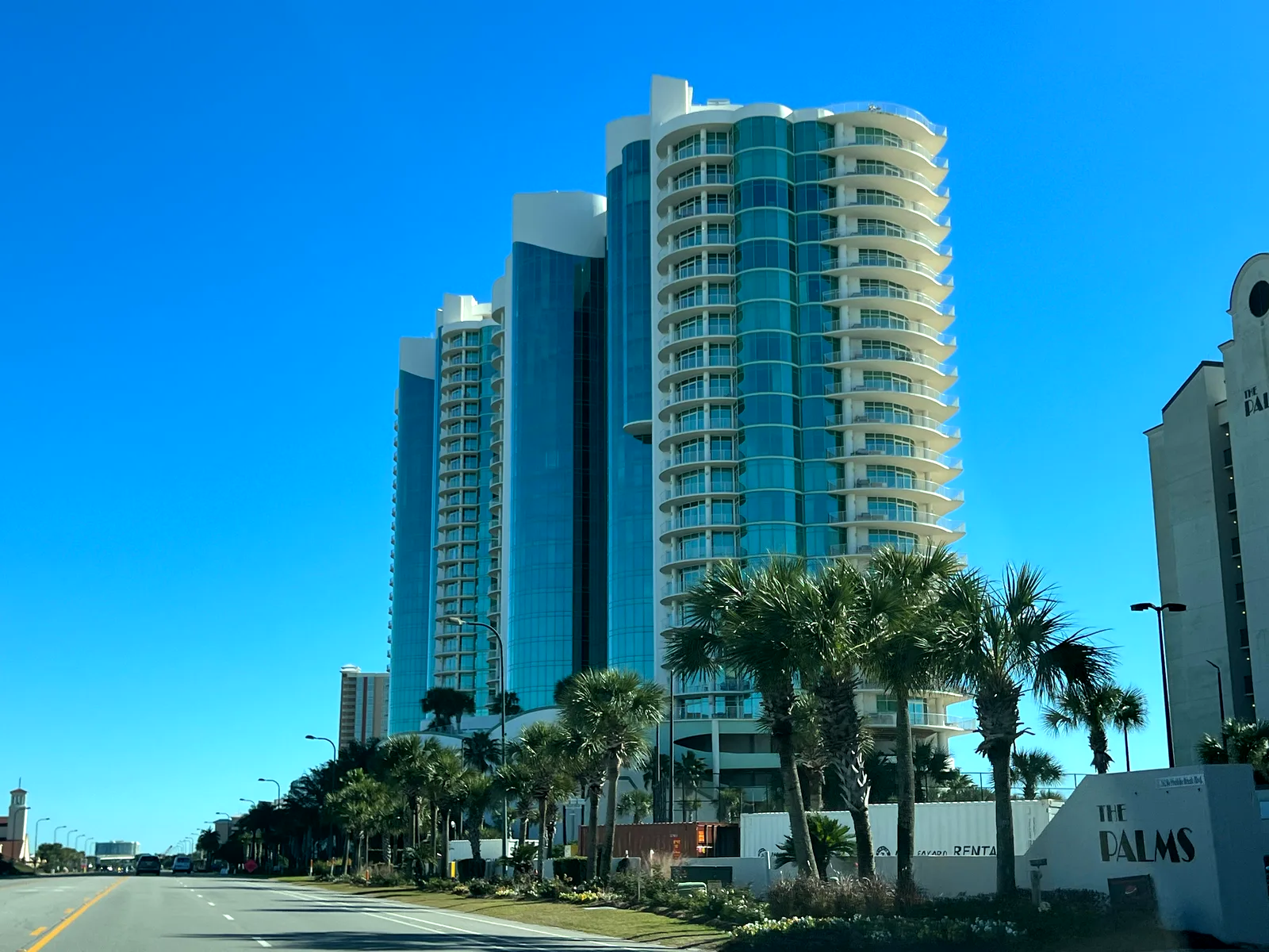 Torres acristaladas de un hotel de playa vistas desde la avenida, entre palmeras.