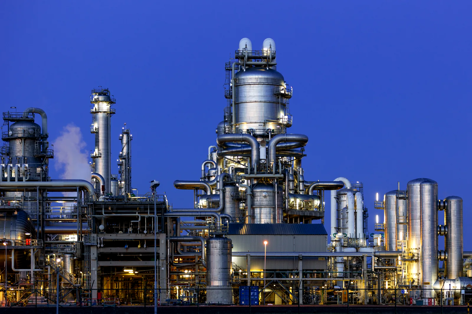 Planta petroquímica iluminada al anochecer, con las torres de proceso en operación continua.