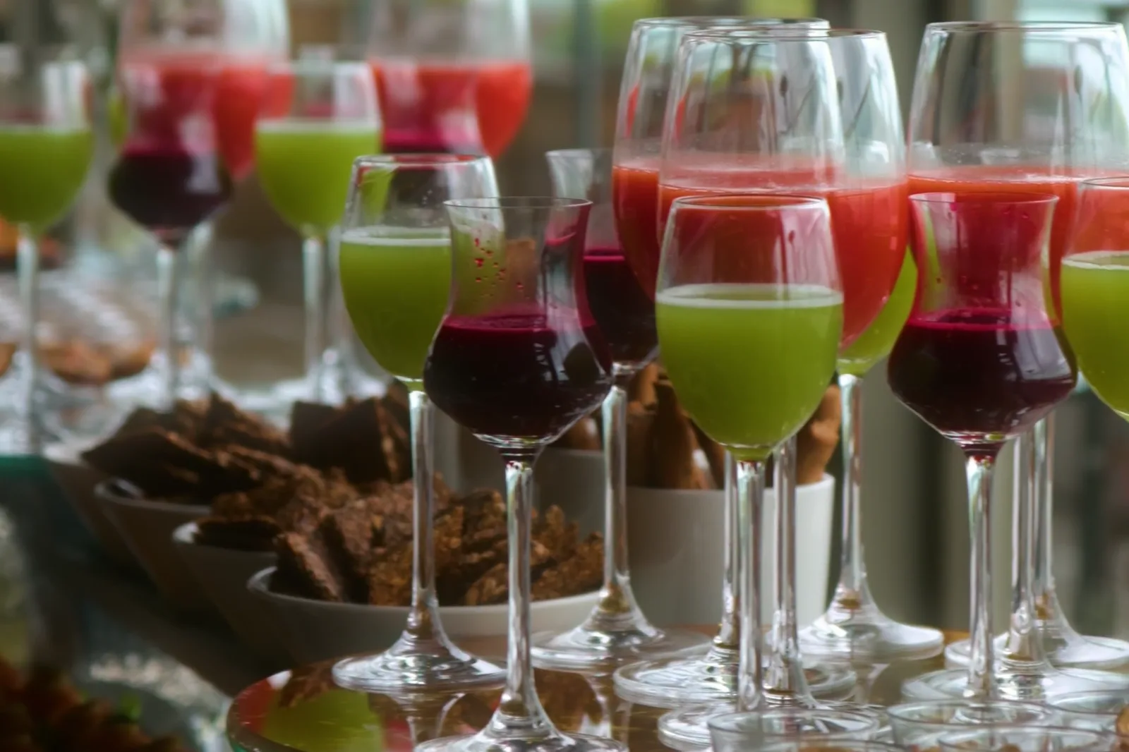 Colourful juices served in glasses on a buffet table by the window.
