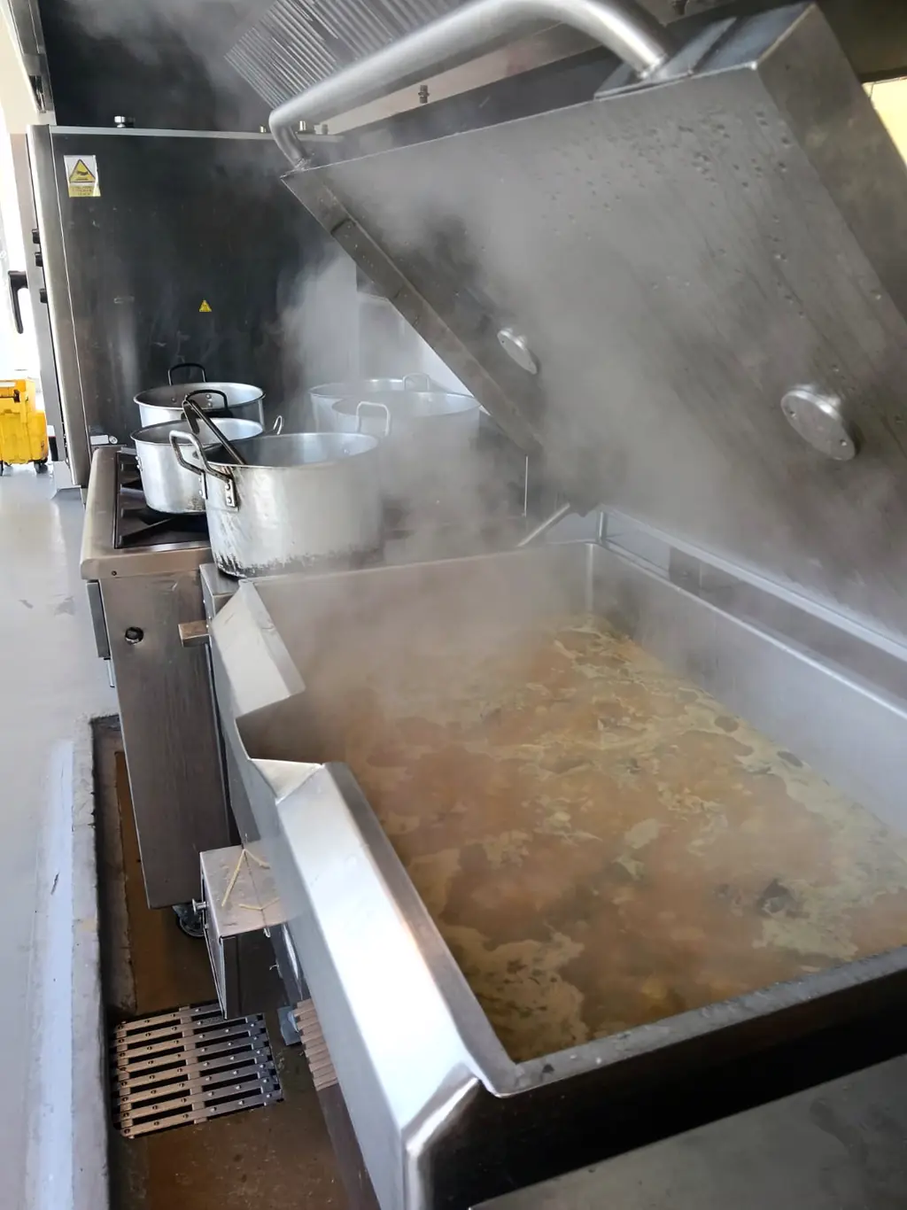 Marmita de vapor en operación con caldo en cocción y ollas de volumen sobre la estufa industrial.