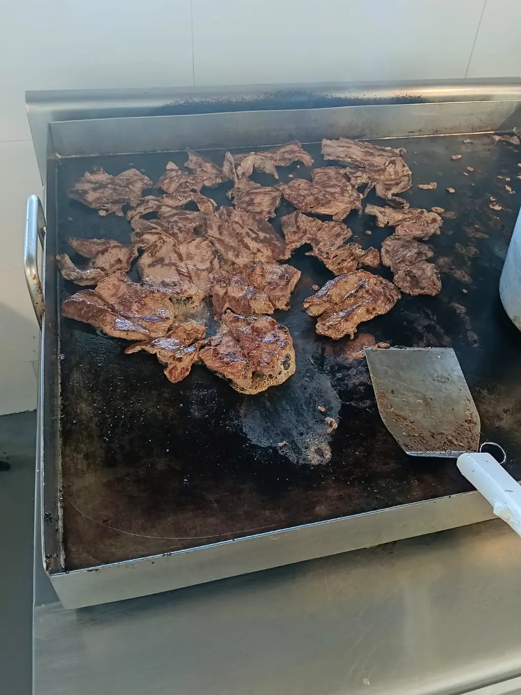 Plancha industrial con proteína en cocción durante la preparación del servicio.