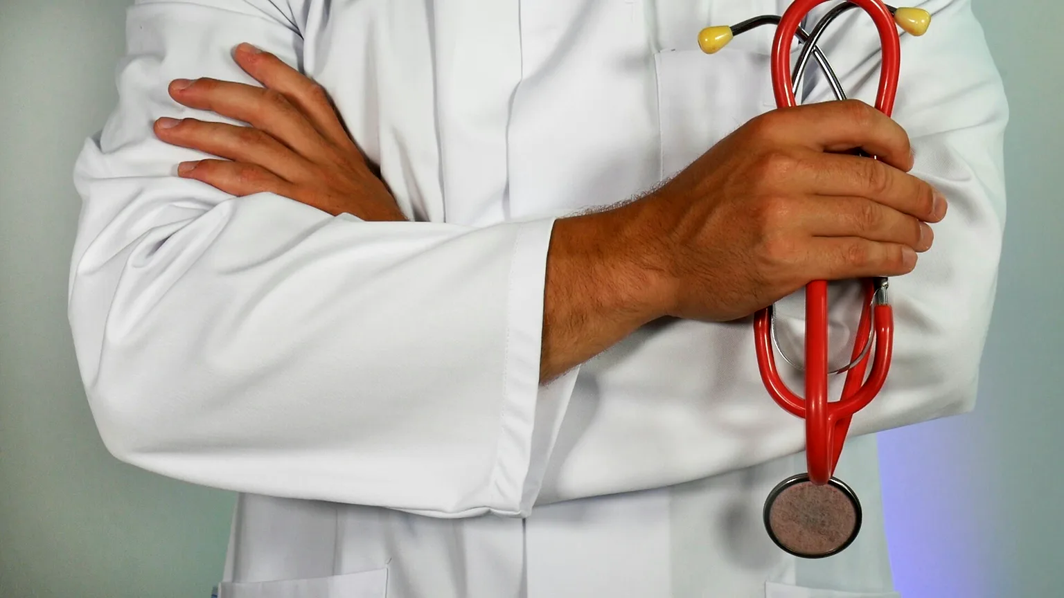 Profesional de la salud con bata blanca y fonendoscopio, de brazos cruzados.