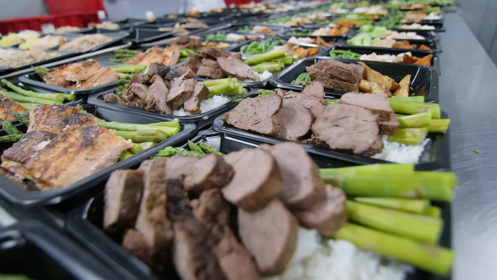 Filas de bandejas de comida preparada con proteína, arroz y verdura, listas para distribución.