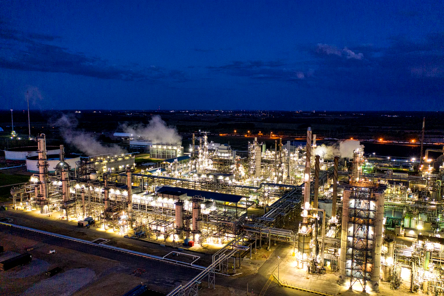Vista aérea nocturna de una planta industrial iluminada, en plena operación de turno.