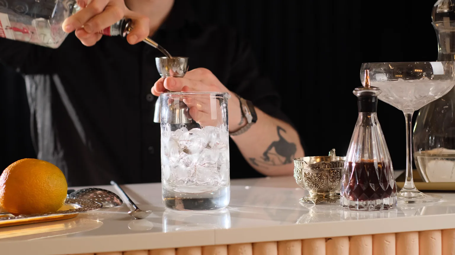 Preparación de un cóctel en barra: vertido sobre vaso mezclador con hielo, con la cristalería dispuesta al lado.